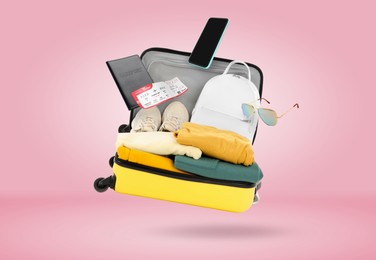 Image of Suitcase, clothes and other items in air on pink background. Ready to travel