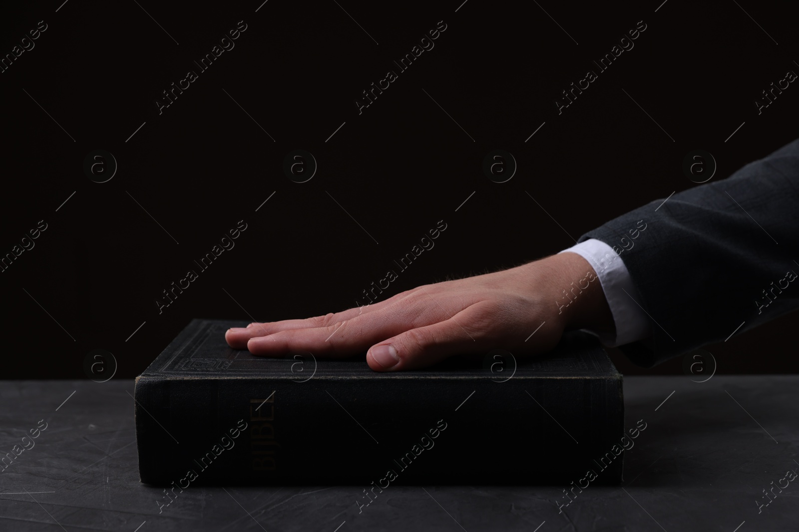 Photo of Man taking oath with his hand on Bible at black table, closeup