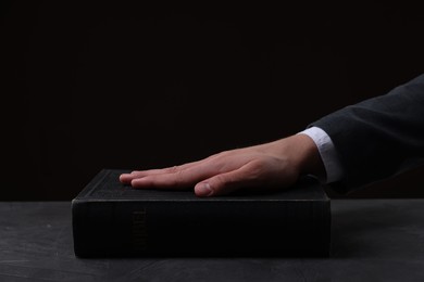 Man taking oath with his hand on Bible at black table, closeup