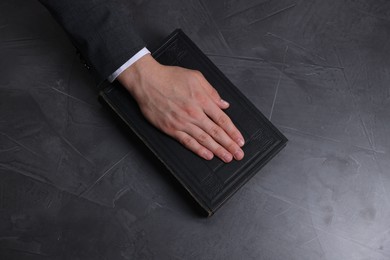 Photo of Man taking oath with his hand on Bible at black table, above view