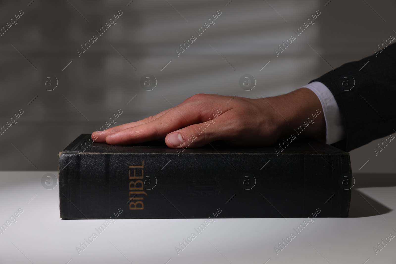 Photo of Man taking oath with his hand on Bible at white table, closeup