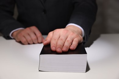 Photo of Man taking oath with his hand on Bible at white table, closeup