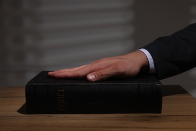 Photo of Man taking oath with his hand on Bible at wooden table, closeup