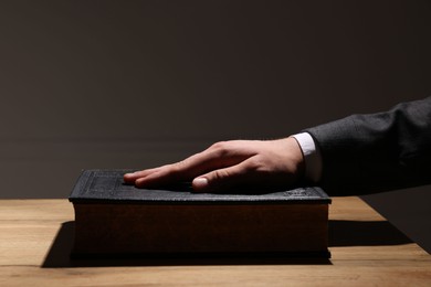 Man taking oath with his hand on Bible at wooden table, closeup