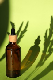 Photo of Bottles of skin care product on light green background with beautiful shadows