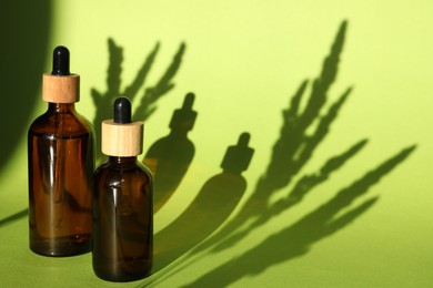 Photo of Bottles of skin care product on light green background with beautiful shadows