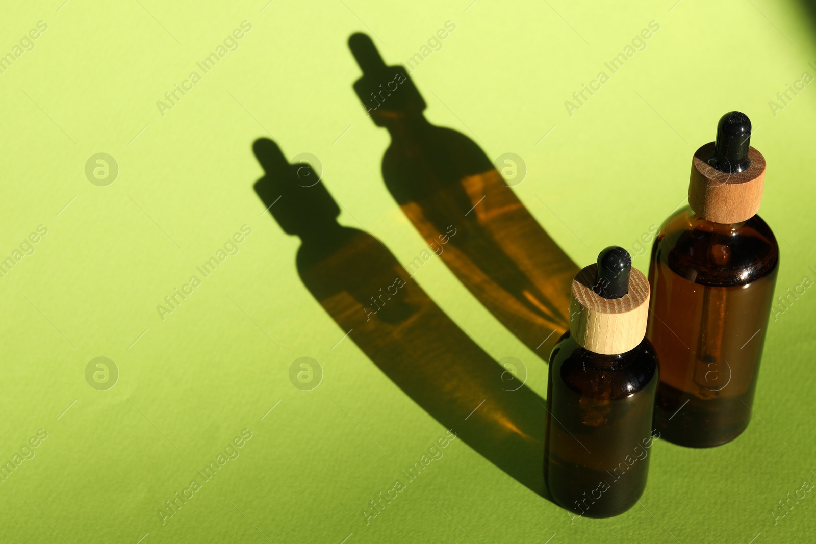 Photo of Bottles of skin care product casting shadows on light green background