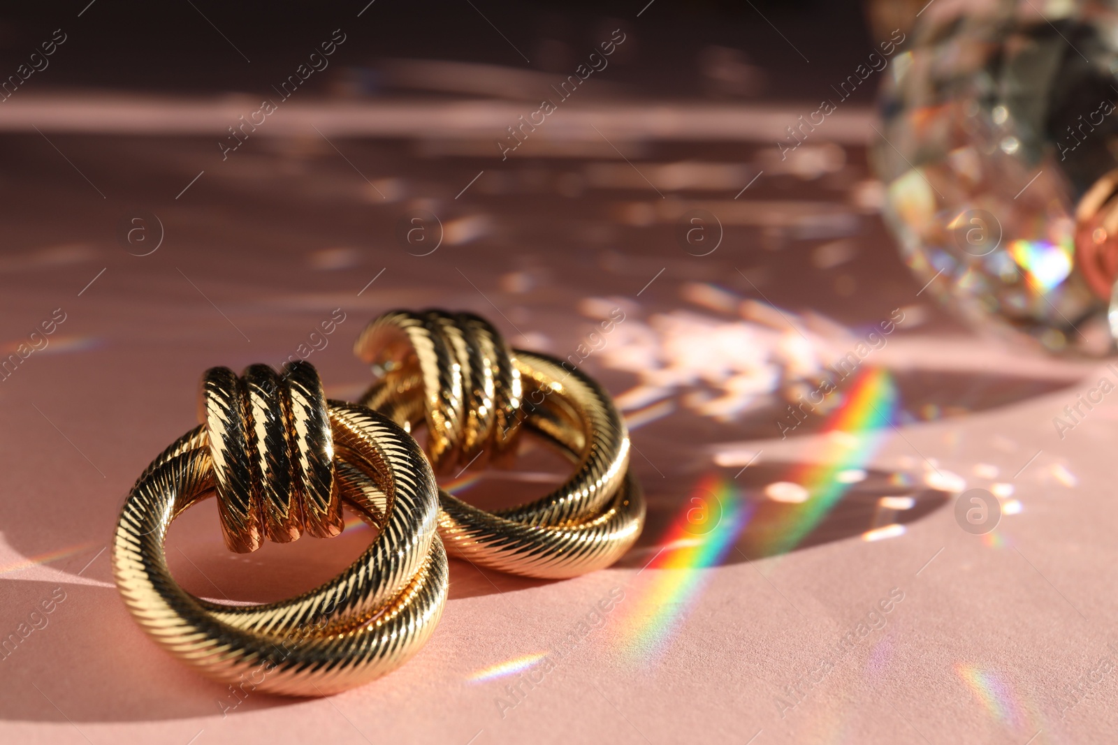 Photo of Beautiful golden earrings on light pink background under sunrays, closeup