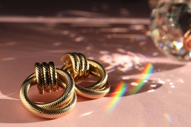 Photo of Beautiful golden earrings on light pink background under sunrays, closeup