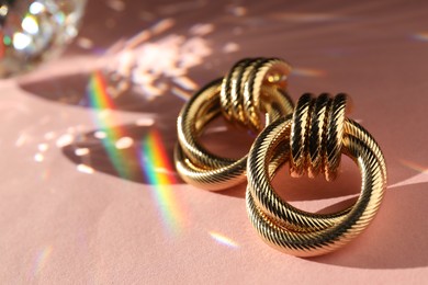 Photo of Beautiful golden earrings on light pink background under sunrays, closeup