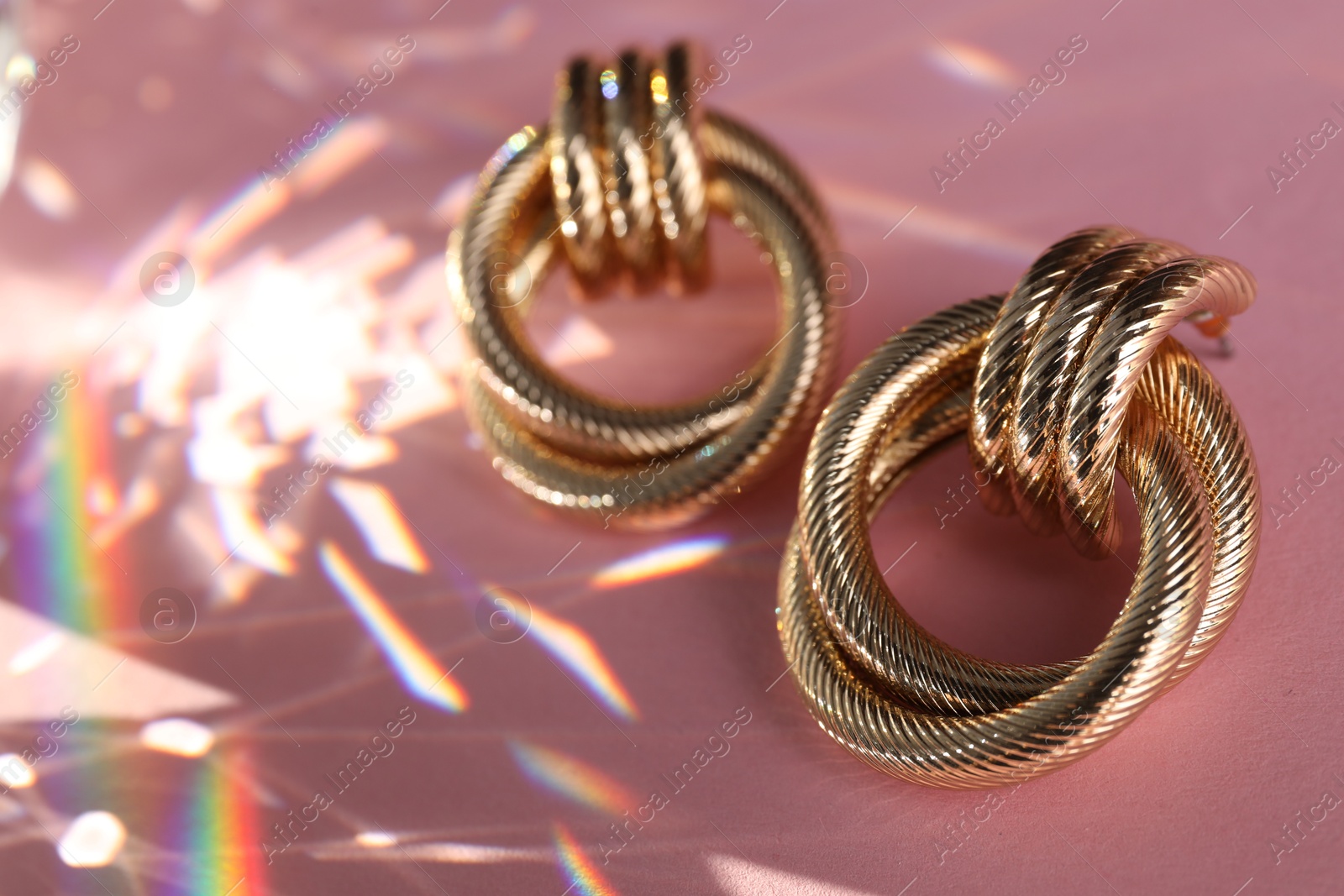 Photo of Beautiful golden earrings on light pink background under sunrays, closeup