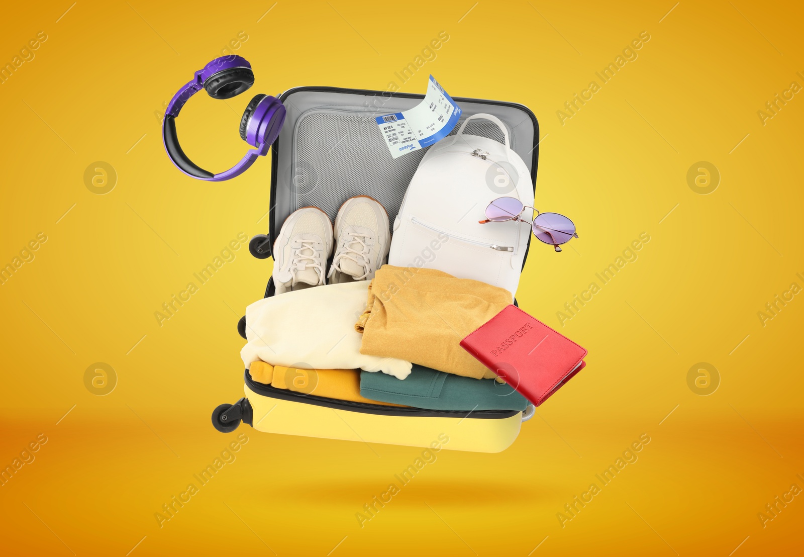 Image of Suitcase, clothes and other items in air on orange background. Ready to travel