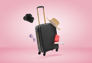 Image of Suitcase, passport, ticket, hat, sunglasses and camera in air on pink background. Ready to travel