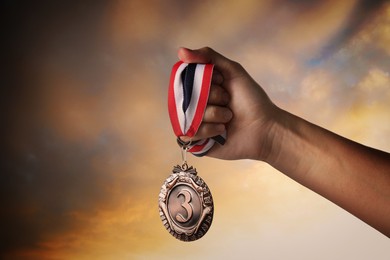 Image of Woman holding bronze medal in hand against sunset sky, closeup