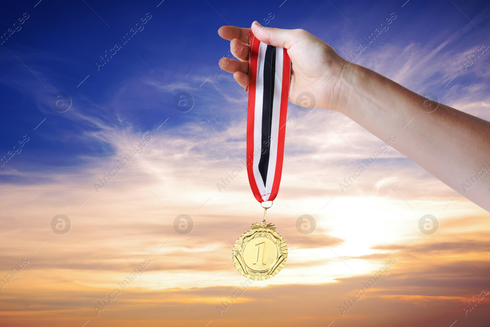 Image of Woman holding gold medal in hand against sunset sky, closeup