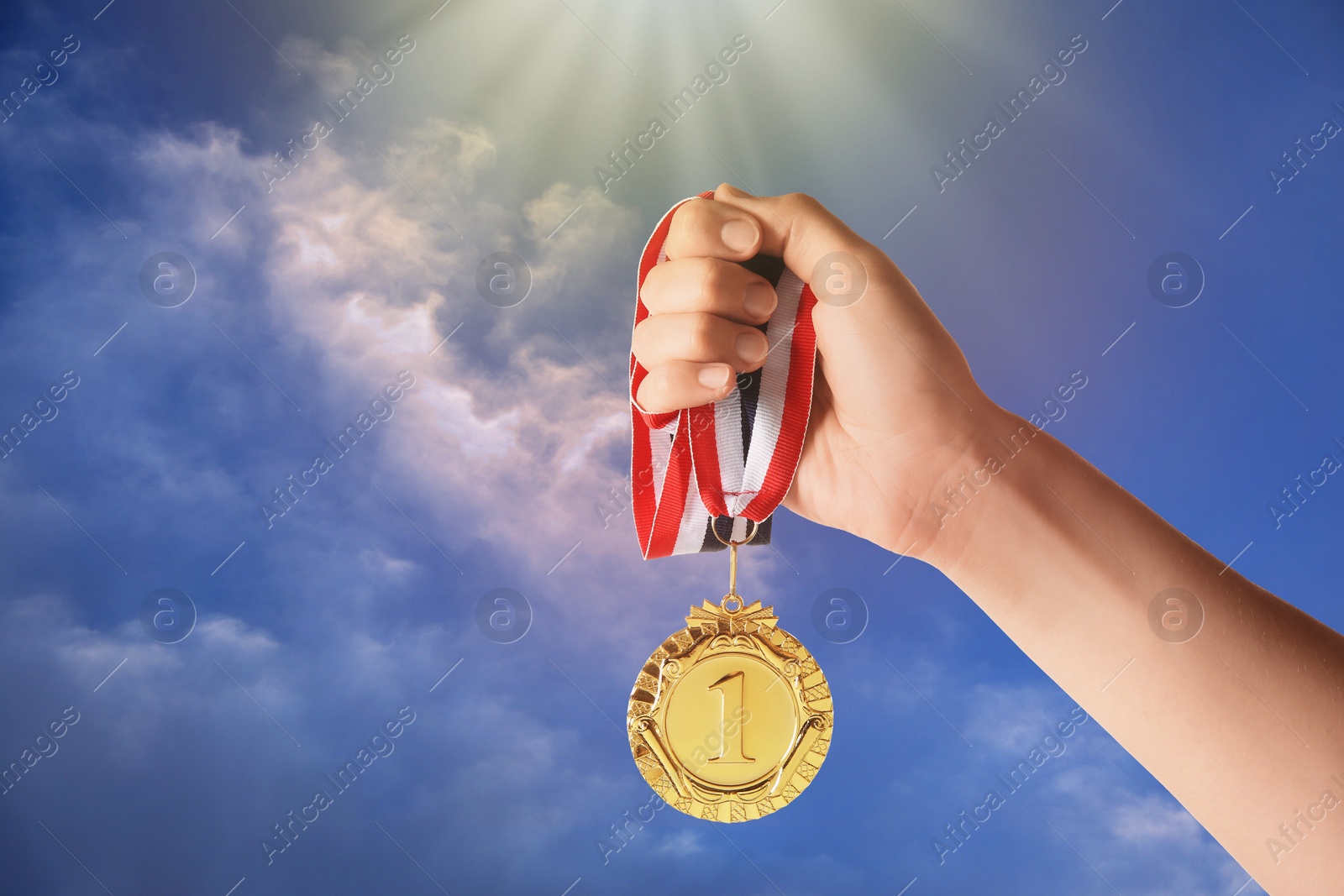 Image of Woman holding gold medal in hand against sky, closeup