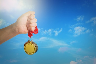 Image of Man holding gold, silver and bronze medals in hand against sky, closeup