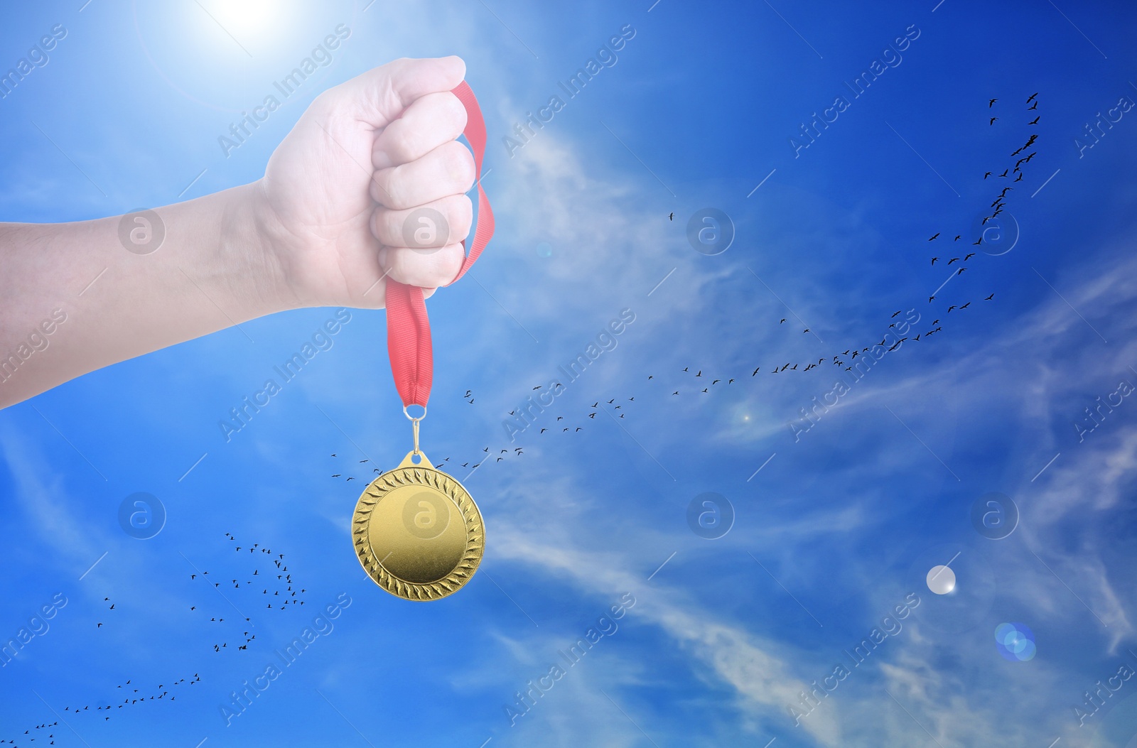 Image of Man holding gold medal in hand against sky, closeup