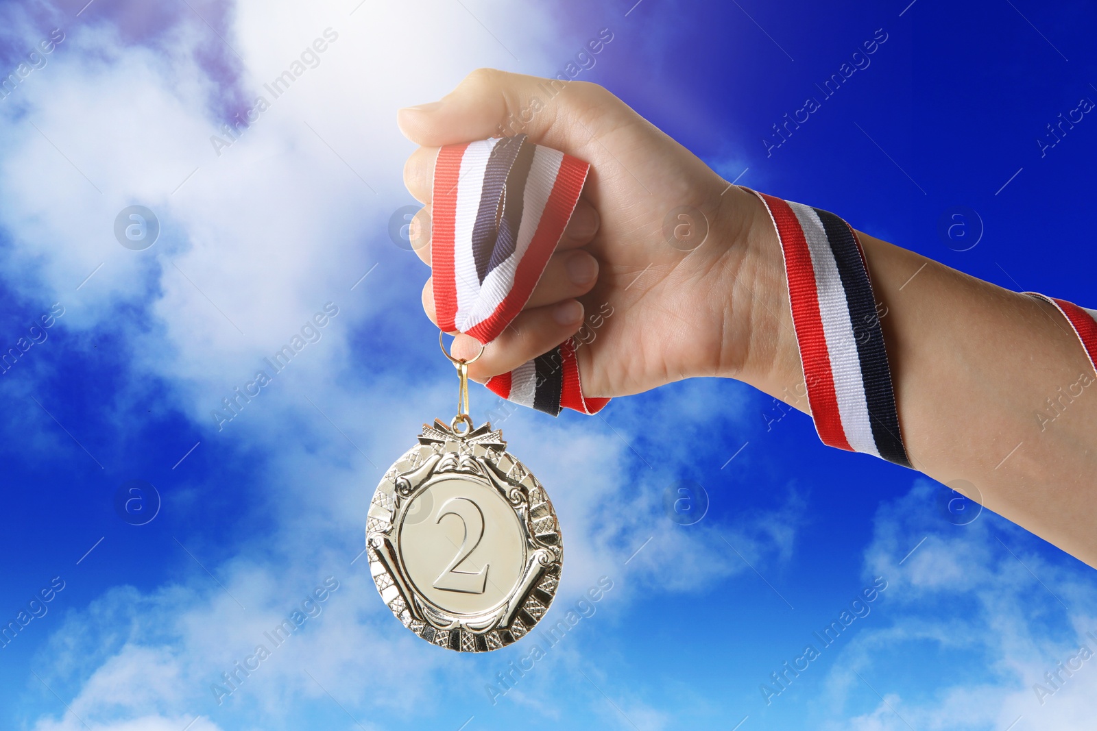 Image of Woman holding silver medal in hand against sky, closeup