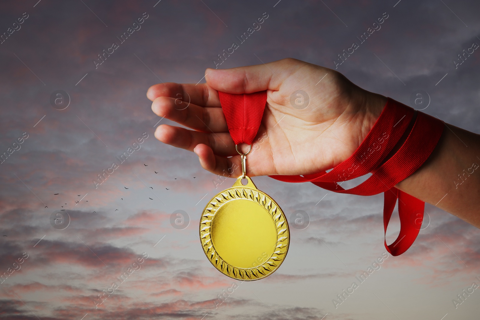 Image of Woman holding gold medal in hand against sunset sky, closeup