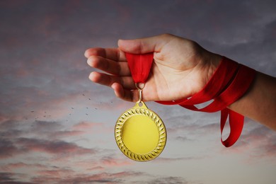 Image of Woman holding gold medal in hand against sunset sky, closeup