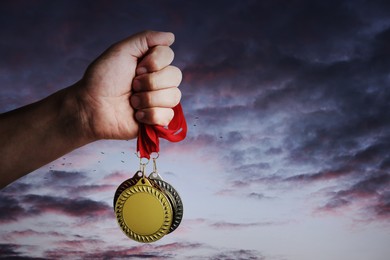 Image of Man holding gold, silver and bronze medals in hand against sunset sky, closeup