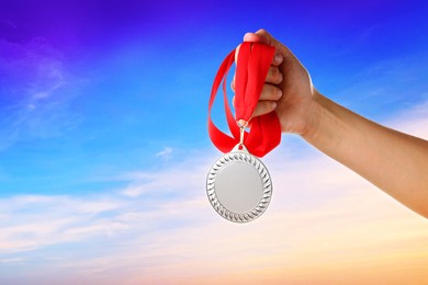 Image of Woman holding silver medal in hand against sky, closeup