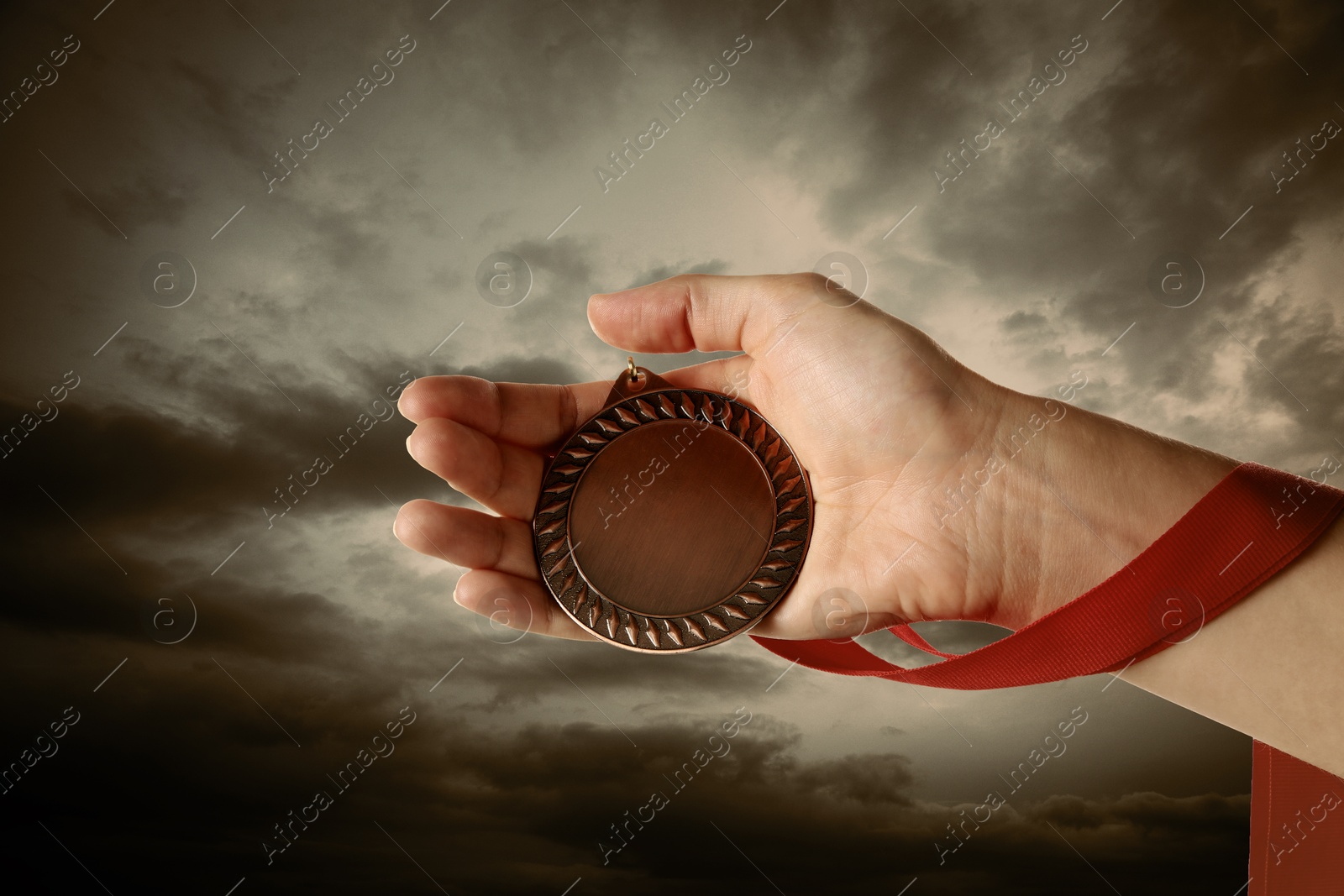 Image of Woman holding bronze medal in hand against sunset sky, closeup