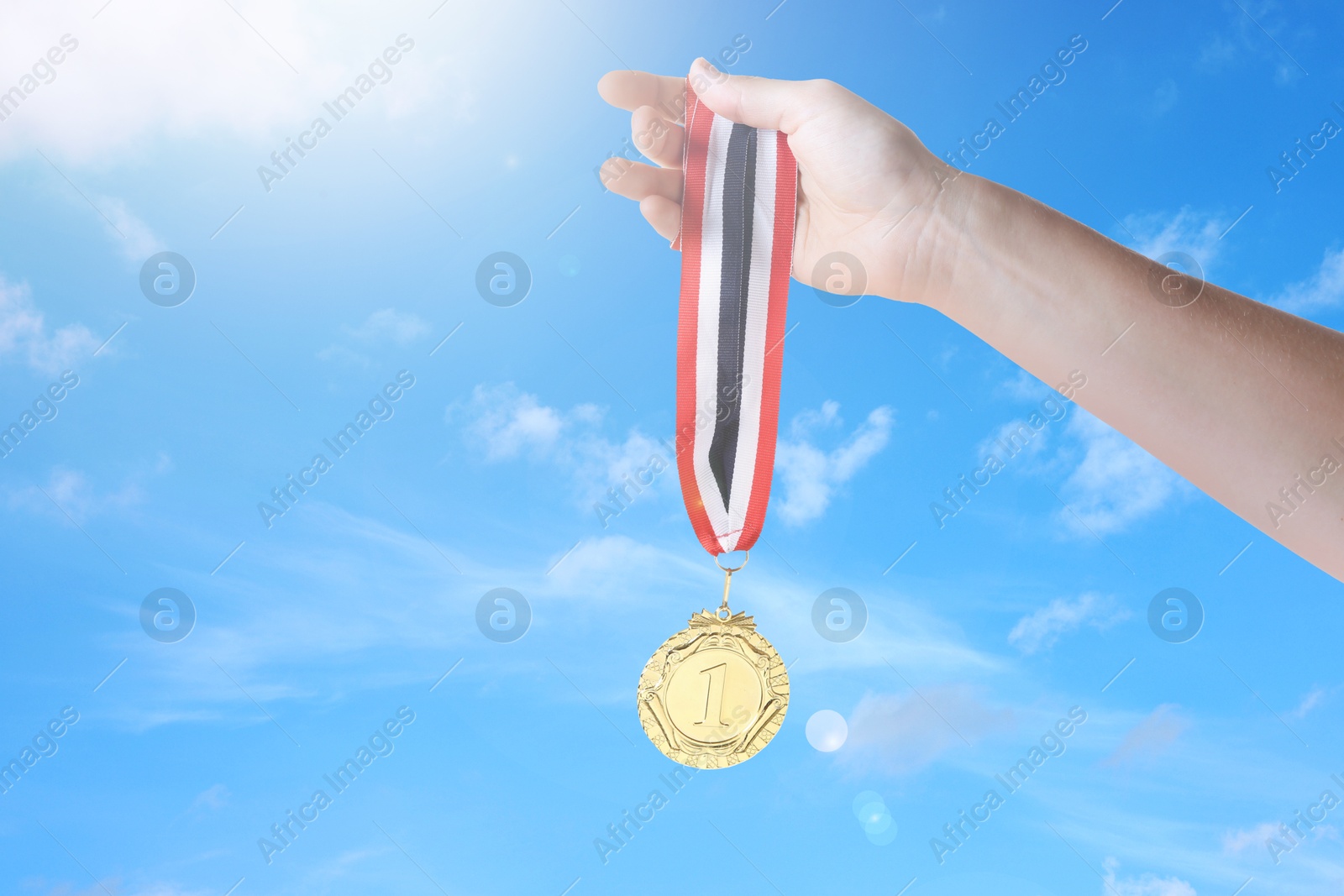 Image of Woman holding gold medal in hand against sky, closeup