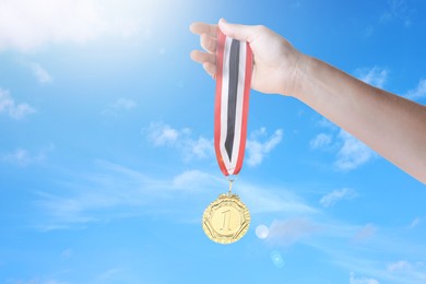 Image of Woman holding gold medal in hand against sky, closeup