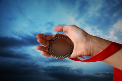 Image of Woman holding bronze medal in hand against sky, closeup