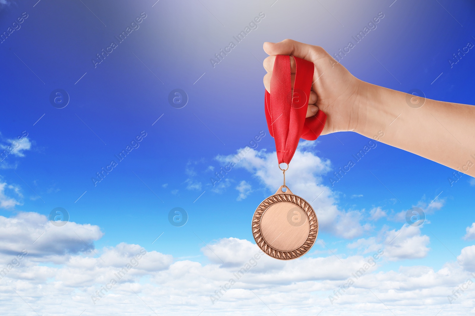 Image of Woman holding bronze medal in hand against sky, closeup