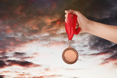 Image of Woman holding bronze medal in hand against sunset sky, closeup