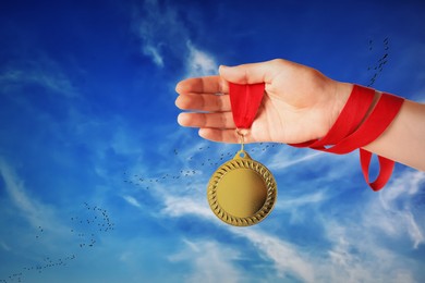 Image of Woman holding gold medal in hand against sky, closeup