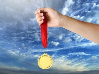 Image of Woman holding gold medal in hand against sky, closeup