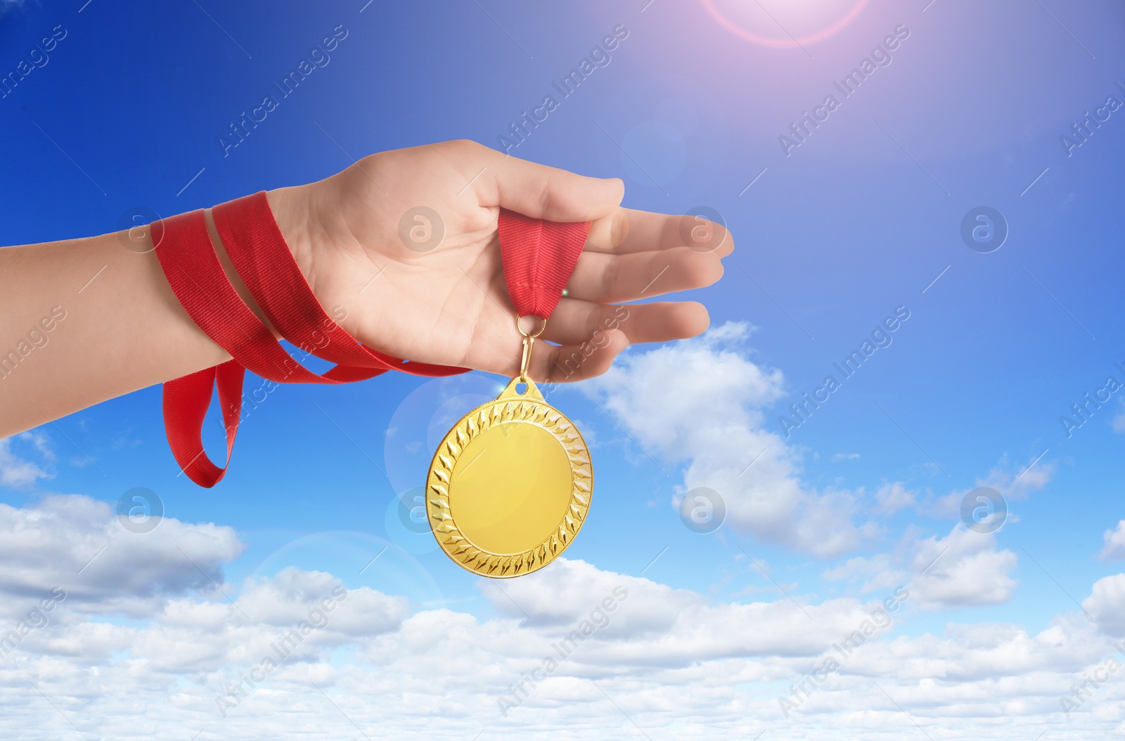 Image of Woman holding gold medal in hand against sky, closeup