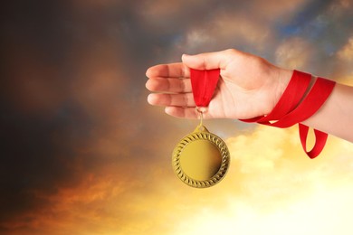 Image of Woman holding gold medal in hand against sunset sky, closeup