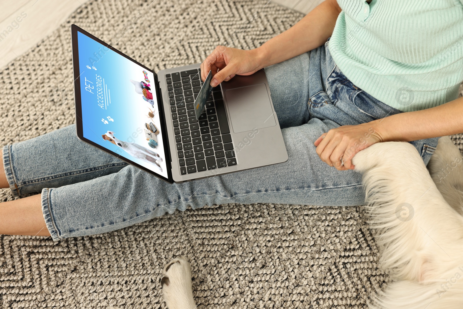 Image of Woman holding her dog's paw while shopping online on laptop at home, closeup. Computer with open pet shop website