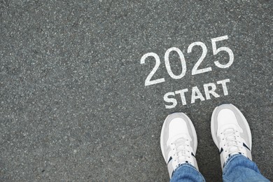 Image of Man standing near sign 2025 Start on asphalt, top view. Concept of new year, fresh beginning