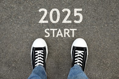 Image of Man standing near sign 2025 Start on asphalt, top view. Concept of new year, fresh beginning