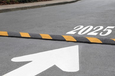 Image of Arrow pointing at sign 2025 behind speed bump on asphalt road. Concept of new year, fresh beginning