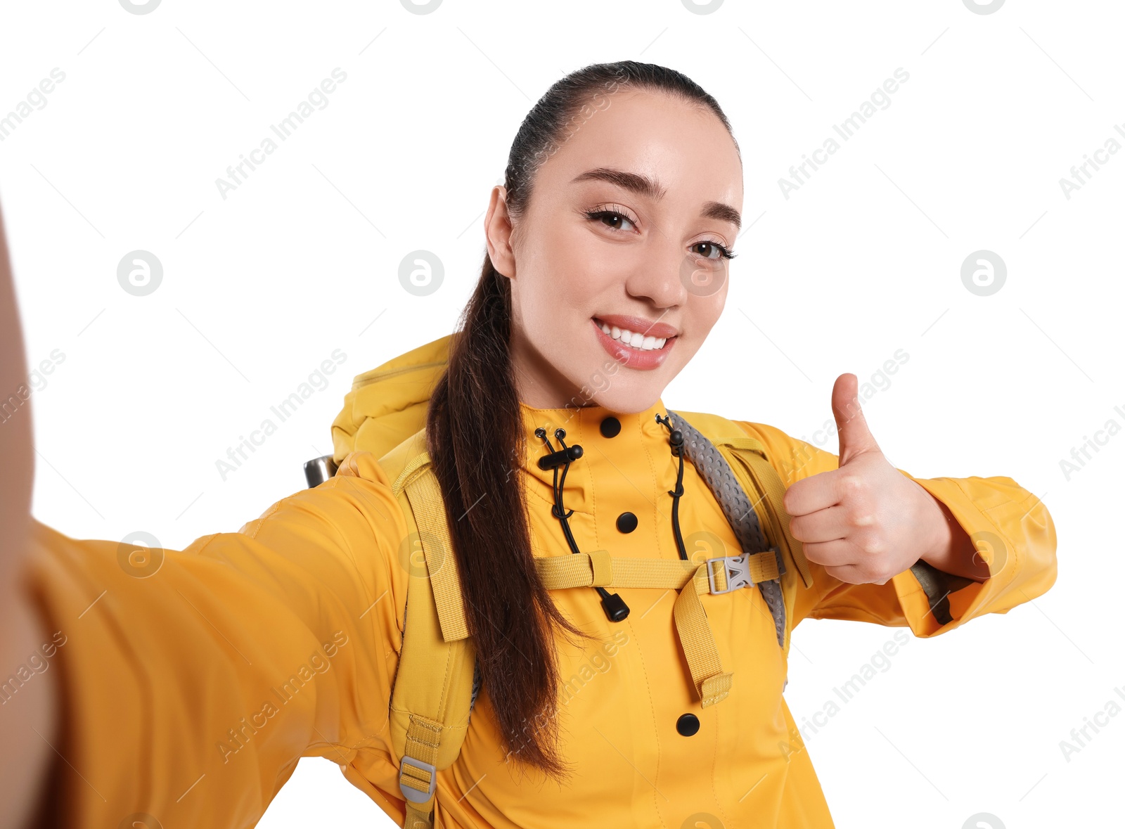 Photo of Smiling young woman with backpack taking selfie and showing thumb up on white background. Active tourism