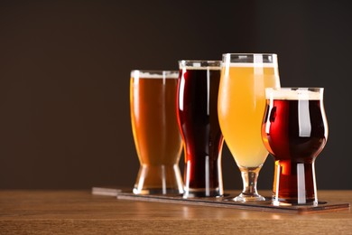 Photo of Glasses with different types of beer on wooden table against dark background, space for text