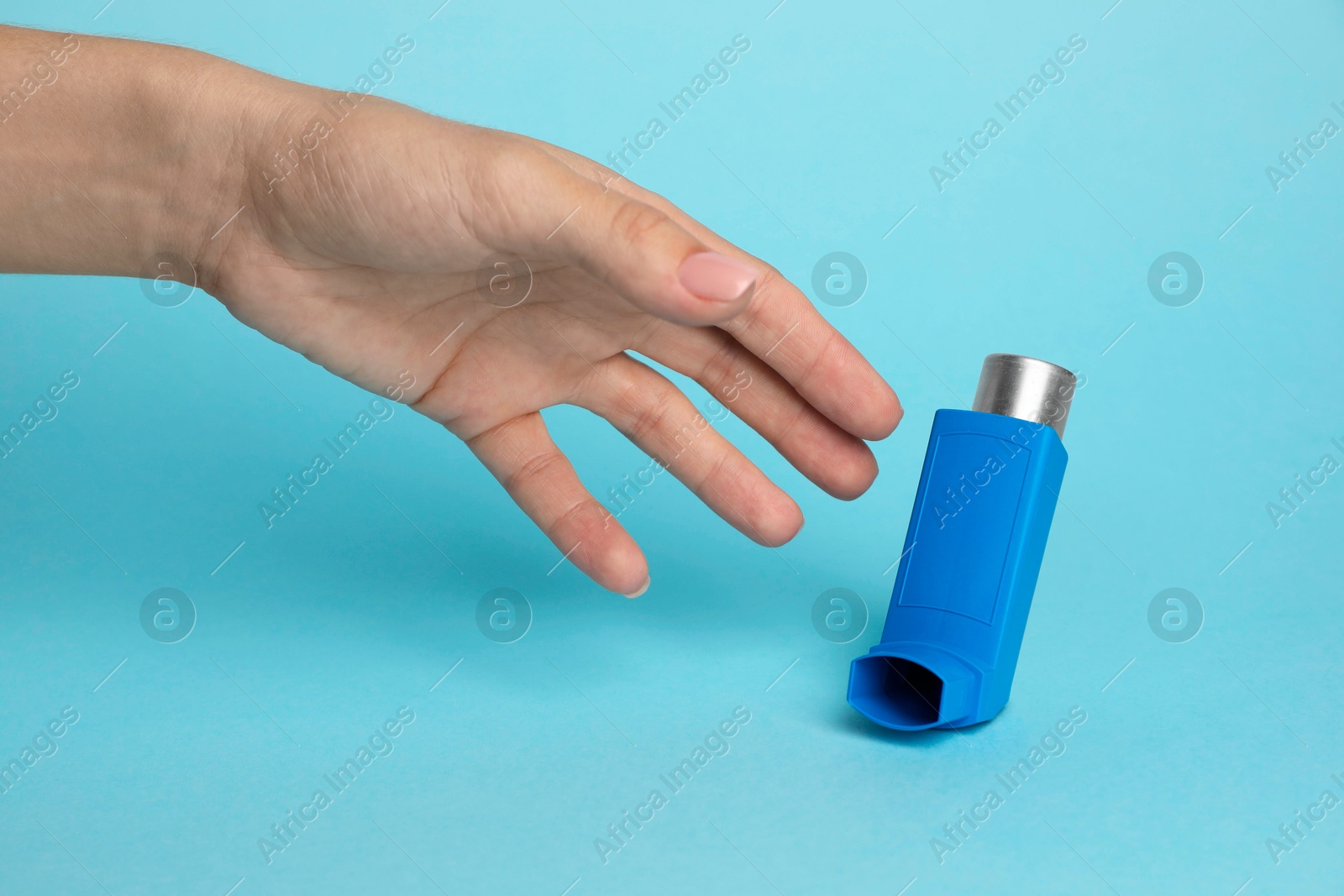 Photo of Woman reaching for asthma inhaler on light blue background, closeup