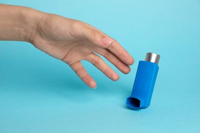 Photo of Woman reaching for asthma inhaler on light blue background, closeup