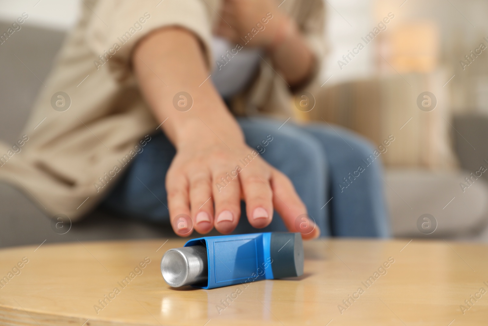 Photo of Woman reaching for asthma inhaler at wooden table indoors, closeup