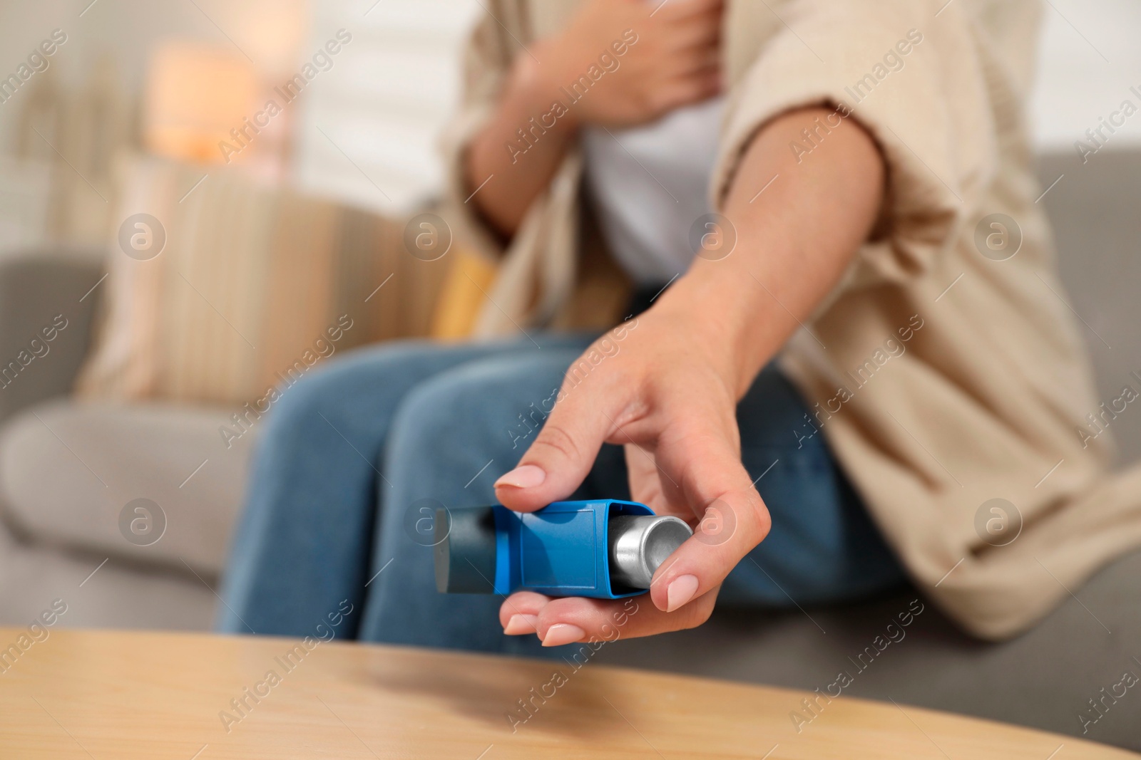 Photo of Woman holding asthma inhaler at wooden table indoors, closeup