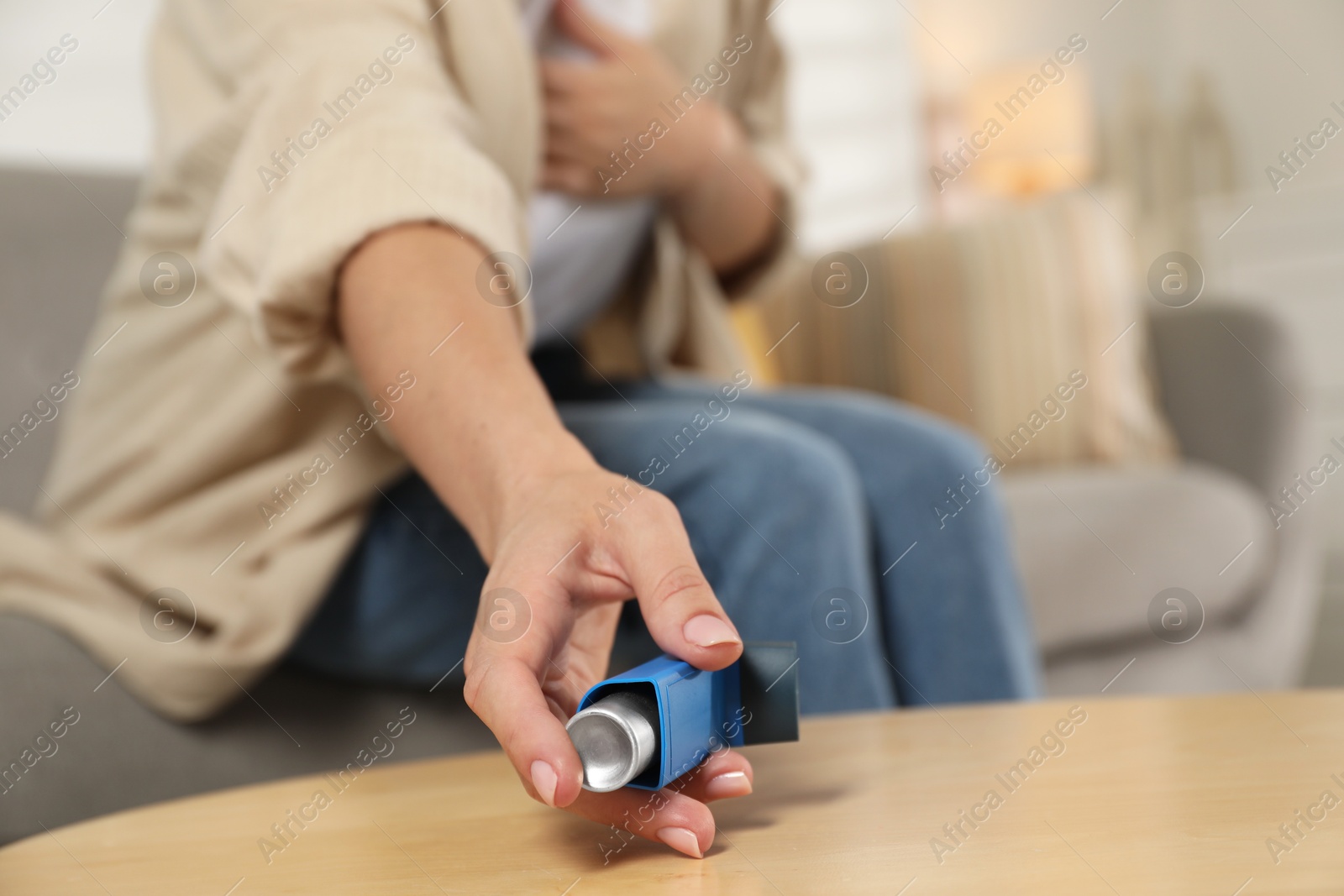 Photo of Woman holding asthma inhaler at wooden table indoors, closeup