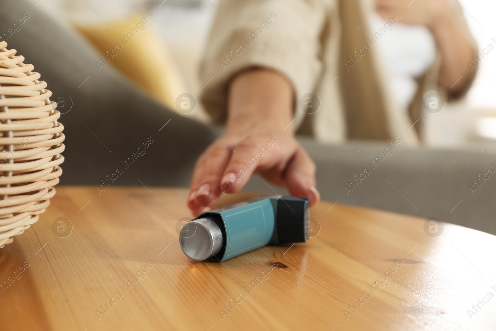 Photo of Woman reaching for asthma inhaler at wooden table indoors, closeup