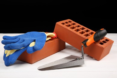 Photo of Red bricks, gloves and trowel on white wooden table. Building material and construction tools